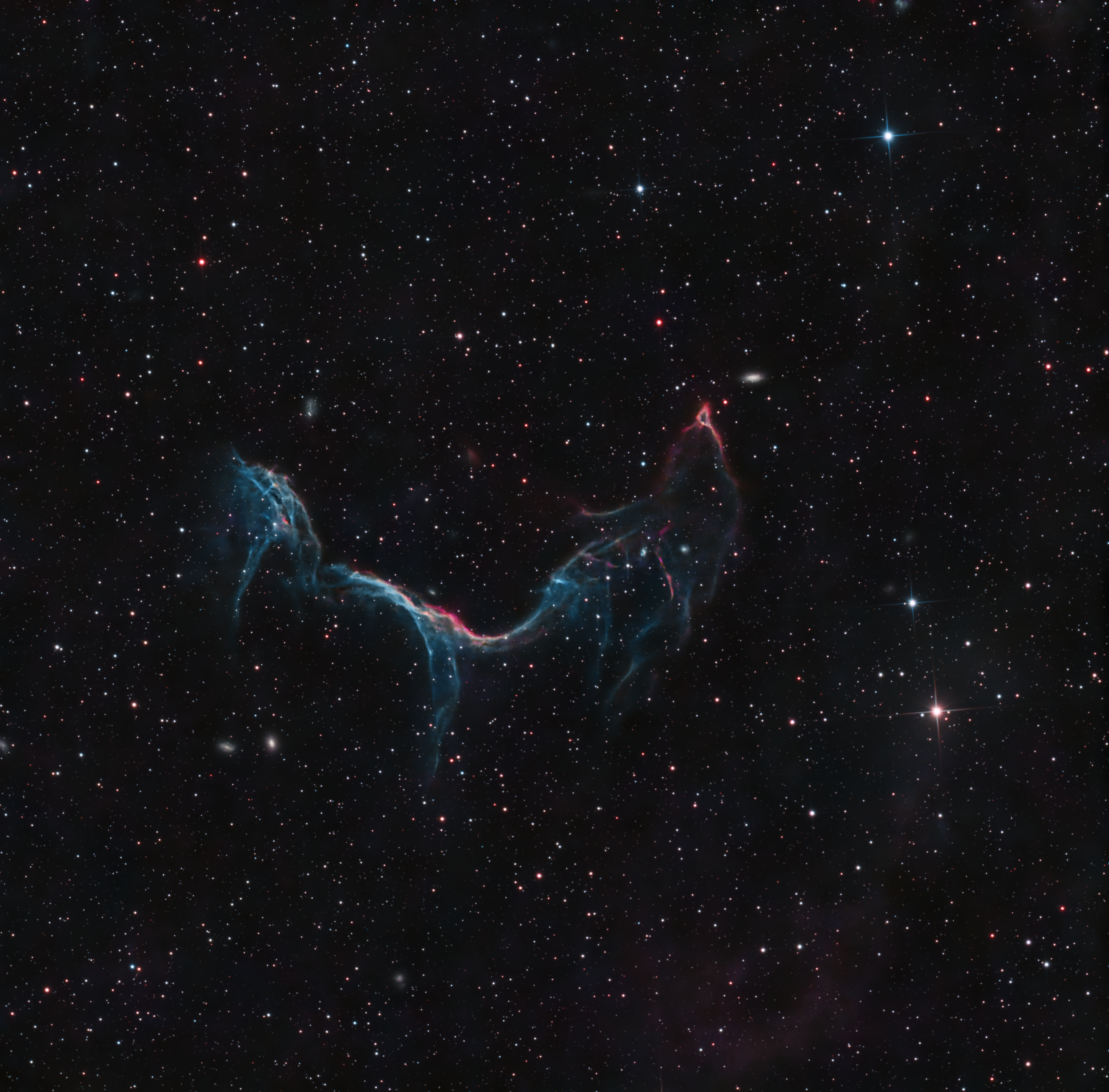 A thin blue and red supernova-remnant arc crossing a dark field of stars.