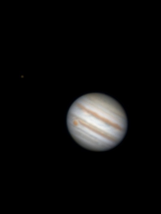 A small telescopic view of Jupiter showing pale cloud bands against black space.
