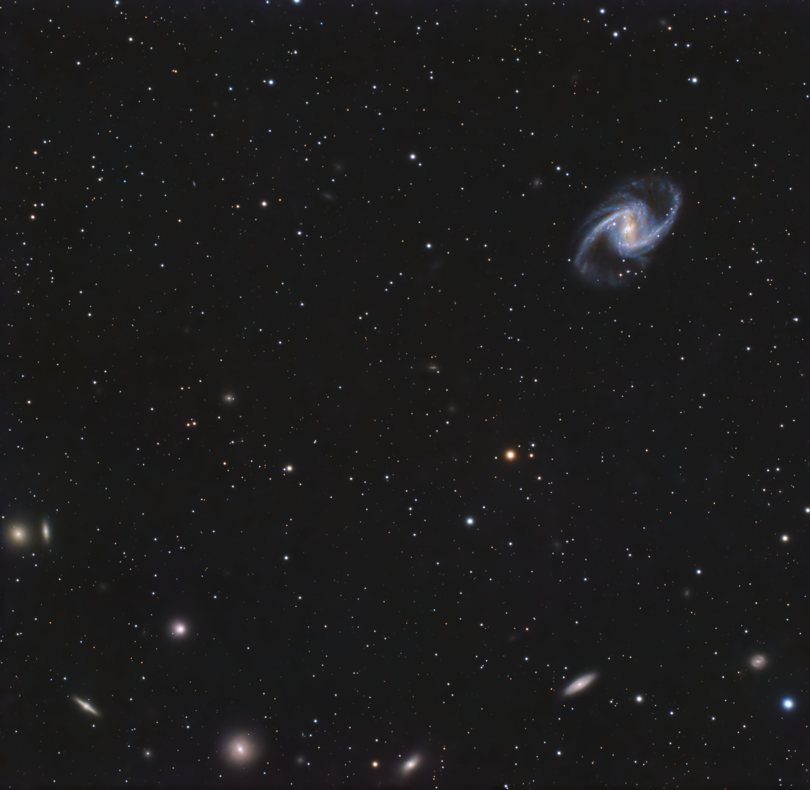 The bright central bar and blue spiral arms of NGC 1365 in the upper right of a wide star field with smaller galaxies.